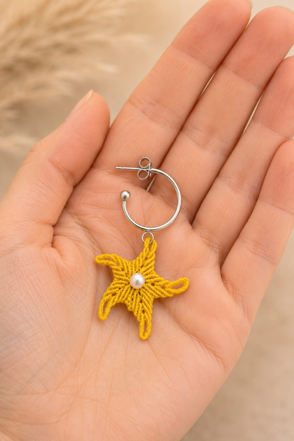 Boucle d'oreille étoile de mer en micro-macramé tenue dans une main, taille réelle du bijou