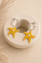 Paire de boucles d'oreilles étoile de mer en micro-macramé jaune posée sur un galet beige, décor pampas